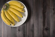 A bunch of bananas in a white plate on a rustic brown wooden table.