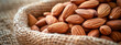 A close-up of raw almonds spilling from a rustic burlap sack onto a wooden table, highlighting natural textures and healthy snacking.
