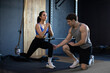 Young woman doing lunges with suspension cable, concentrated male instructor helping lady during workout in modern gym interior