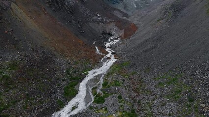 Wall Mural - The aerial view of Chalaadi Glacier. Stormy mountain river. Cloudy summer day. Concept of nature and travel vacation. Mestia, Georgia A valley among high mountains. Boulders and stones. Flight over