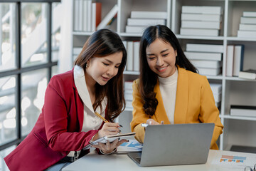 Wall Mural - Cheerful business people using a laptop in an office, happy young entrepreneurs smiling while working together in a modern workspace, Two young business people sitting together at a table.