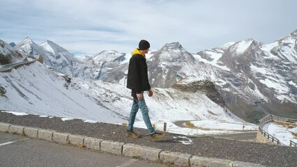 Wall Mural - Man traveler walks along Majestic Grossglockner Mountain Road in Austria, snow covered sharp peaks of the alpine mountains on background. Incredibly beautiful views in the Alpine mountains. Route in