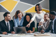 © gstockstudio - Smiling young business team looking at laptop while having group meeting in the office together