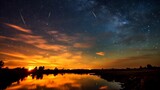 Fototapeta Krajobraz - Starfall against the backdrop of the sunset sky over a quiet river surface