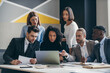 © gstockstudio - Group of confident young business people looking at laptop while working at the modern office