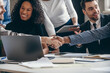 © gstockstudio - Close-up of businessmen shaking hands while sitting with their colleagues at the office desk