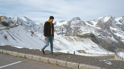 Wall Mural - Man traveler walks along Majestic Grossglockner Mountain Road in Austria, snow covered sharp peaks of the alpine mountains on background. Incredibly beautiful views in the Alpine mountains. Route in