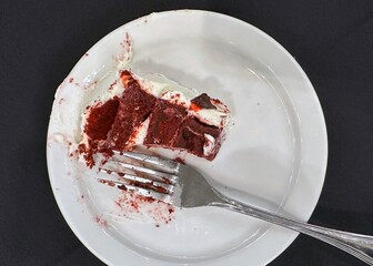 Partially eaten piece of red velvet cake on a white plate with fork