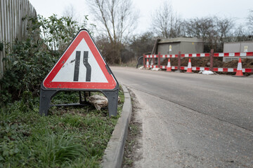 Shallow focus of a British restricted access sign seen on a grass verge at a dangerous road corner. Gas pipes are being laid.