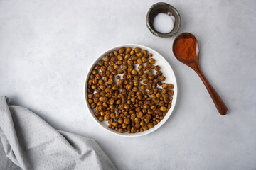 Roasted chickpeas with smoked paprika and salt on a light background in a white plate. View from above. Healthy seasoned chickpeas with various spices