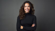 © Studio Nova - Woman with curly hair is smiling and posing confidently with her arms crossed, wearing a black turtleneck against a neutral gray background.