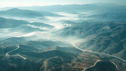 Wall Mural -  an aerial view of a mountain range with a winding road in the foreground and a foggy valley in the far distance with a bird's eye view.