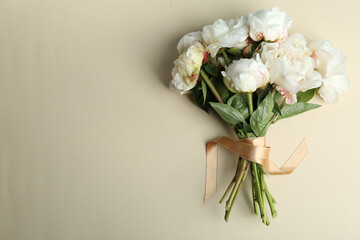 Wall Mural - Bouquet of beautiful peonies with ribbon on beige background, flat lay. Space for text