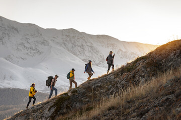 Wall Mural - group of young active hikers with backpacks walks uphill in mountains at sunset
