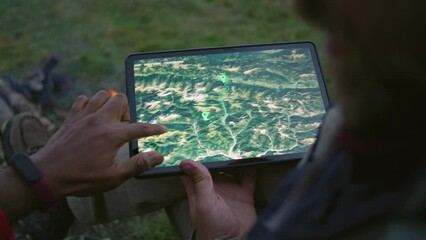Close up of hiking buddies discussing route. African American man checks trail with Caucasian tourist using application with map on tablet computer. Hikers on vacation to mountains. Outdoor activities