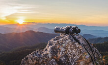Binoculars On Top Of Rock Mountain At Beautiful Sunset Background.