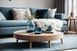 © Basileus - Scandinavian interior home design of modern living room with blue sofa and glass vase on a round wooden table near the window