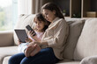 © fizkes - Young woman and 5s daughter using cellphone and tablet at home Little cute girl holding pad device spend time on internet with mother showing her new mobile app, having fun online. Modern tech overuse
