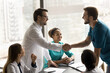 © fizkes - Two happy doctor men celebrating successful collaboration on difficult medical patient case, shaking hands over table, smiling, laughing, meeting with o multiethnic team of colleagues