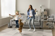 © fizkes - Excited mom and happy preschool daughter kid dancing with playful pet, hopping in living room, having fun, laughing, enjoying active leisure, music at home, training adorable beagle dog. Full length