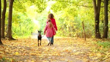 Back Of Girl With Mother Walking With Dog In Autumn Park