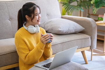 Beautiful young woman in a yellow casual dress enjoying listening to music and smiling while relaxing on the sofa at home. Young woman with headphones uses laptop and smartphone at home. relax concept