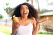 Young African American woman holding an orange juice at outdoors with shocked facial expression