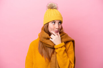 Wall Mural - Young redhead woman wearing winter jacket isolated on pink background having doubts and with confuse face expression