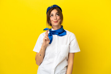 Airplane stewardess woman isolated on yellow background with fingers crossing and wishing the best