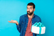 Young handsome man with a big cake over isolated blue background unhappy for not understand something