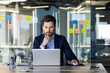 © Liubomir - Mature experienced businessman working inside office with laptop, thinking man reading from screen, financier investor in business suit, boss with beard sitting at table near window with computer.