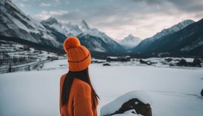 Portrait from the back of the girl traveler in an orange sweater and winter hat in the mountains 