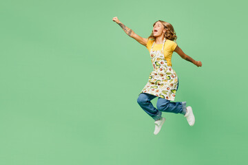 Full body side view young housewife housekeeper chef cook baker woman wear apron yellow t-shirt jump high do super hero gesture pov fly isolated on plain green background studio. Cooking food concept.