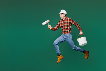 Wall Mural - Full body young employee laborer man wearing red shirt hardhat jump high hold paint roller paint tin isolated on plain green background. Instruments for renovation apartment room. Repair home concept.