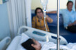© arcyto - Close up set iv fluid intravenous drop saline drip in hospital room with blurry patient woman and caregiver on hospital bed.Medical treatment emergency patient.Caregiver and hopeful concept.