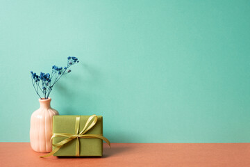 Wall Mural - Khaki gift box with vase of dry flower on red table. mint green wall background