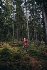 a woman in a pink jacket travels through the mountains. go on a hike with friends. a woman stands in the middle of a spruce forest