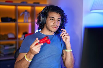 Poster - Young latin man streamer playing video game using joystick at gaming room