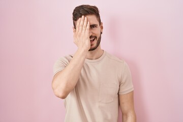 Poster - Hispanic man with beard standing over pink background covering one eye with hand, confident smile on face and surprise emotion.