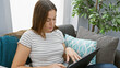 © Krakenimages.com - A young woman browses a tablet while sitting on a cozy sofa in a well-lit living room.