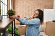 © Krakenimages.com - Young beautiful plus size woman smiling confident putting plant on shelving at new home