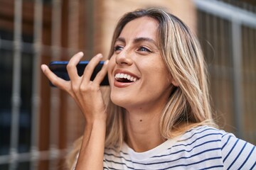 Canvas Print - Young blonde woman miling confident listening audio message by the smartphone at street