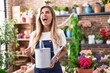 Young blonde woman working at florist shop angry and mad screaming frustrated and furious, shouting with anger looking up.