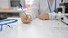 Professional Woman In Lab Coat Writing On A Form, With Microscope And Eyeglasses In A Clinical Laboratory Setting.