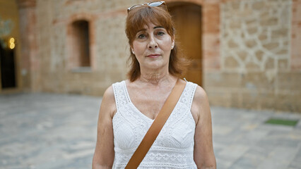 Canvas Print - A mature woman stands confidently on a historic city street, embodying elegance and poise.