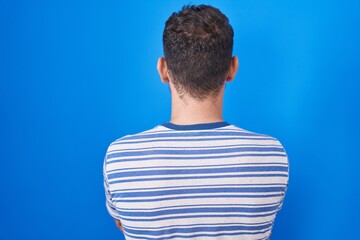 Sticker - Young hispanic man standing over blue background standing backwards looking away with crossed arms