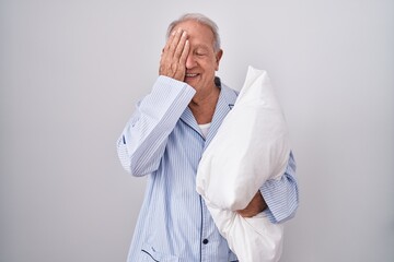 Canvas Print - Senior man with grey hair wearing pijama hugging pillow covering one eye with hand, confident smile on face and surprise emotion.