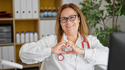 Poster - Middle age hispanic woman doctor smiling doing heart gesture with hands at the clinic