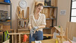 © Krakenimages.com - Blonde woman wearing gloves in a carpentry workshop with wood, tools.