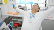 © Krakenimages.com - A mature man in a lab coat stretches with relief in a bright laboratory setting, embodying professional satisfaction.